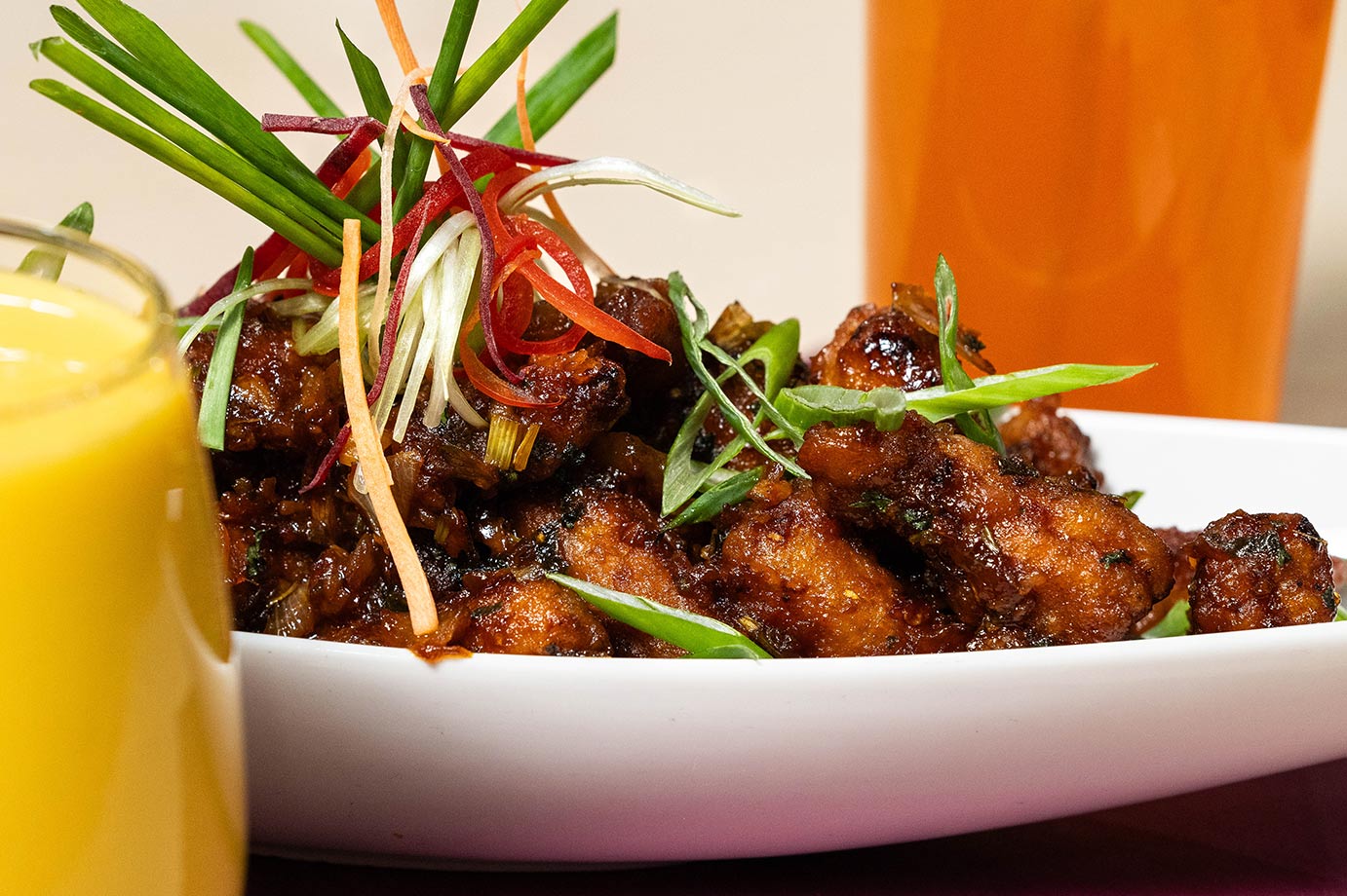 Glazed house appetizer scattered with scallions and julienned vegetables, a mango drink alongside