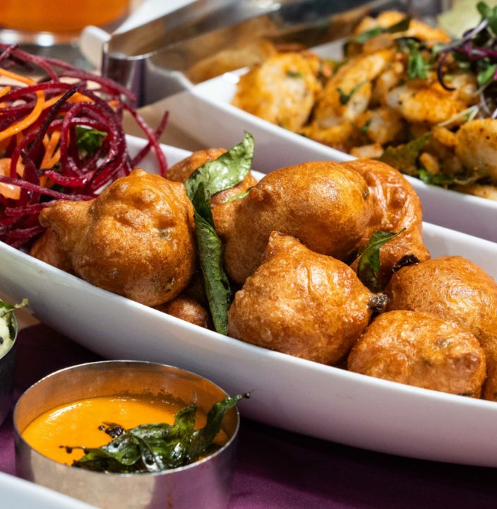 A catering tray of bonda with chutney, and podi idli behind
