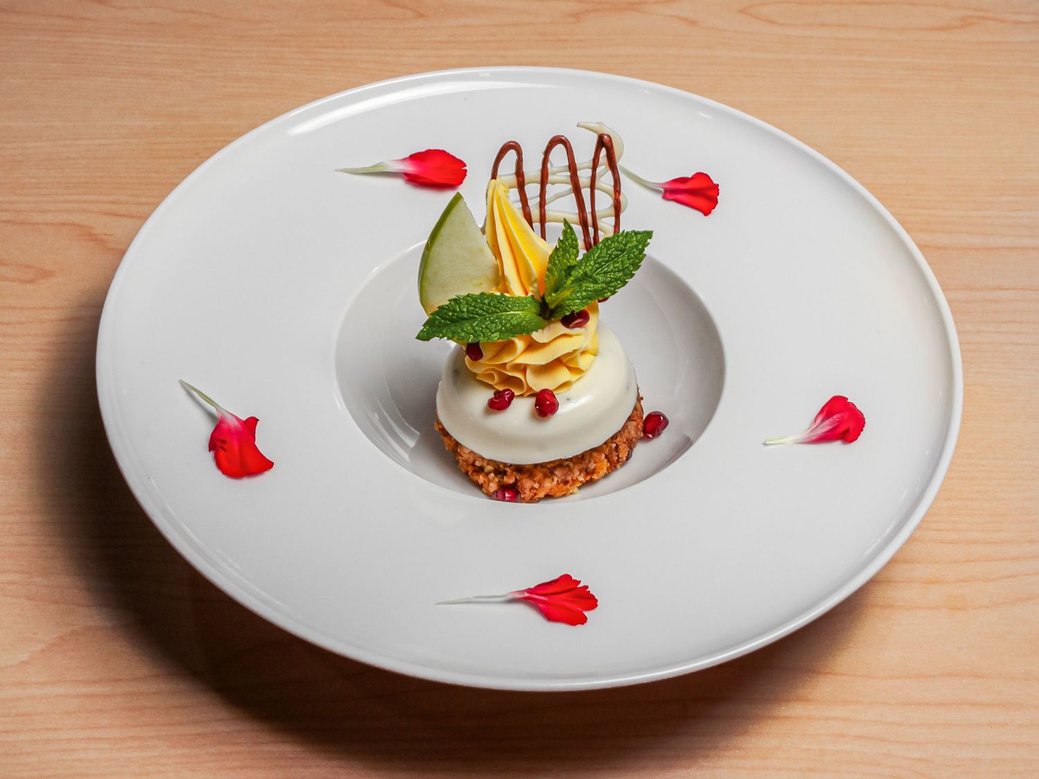 The Coconut Garden dessert — a cream-topped disc with a mango cream rosette, mint, pomegranate and rose petals