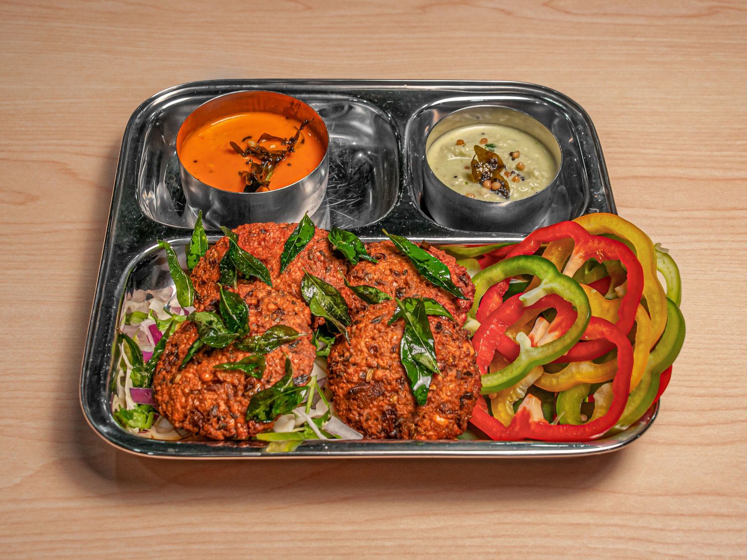 Three masala vada on a steel thali with sambar, coconut chutney and sliced peppers