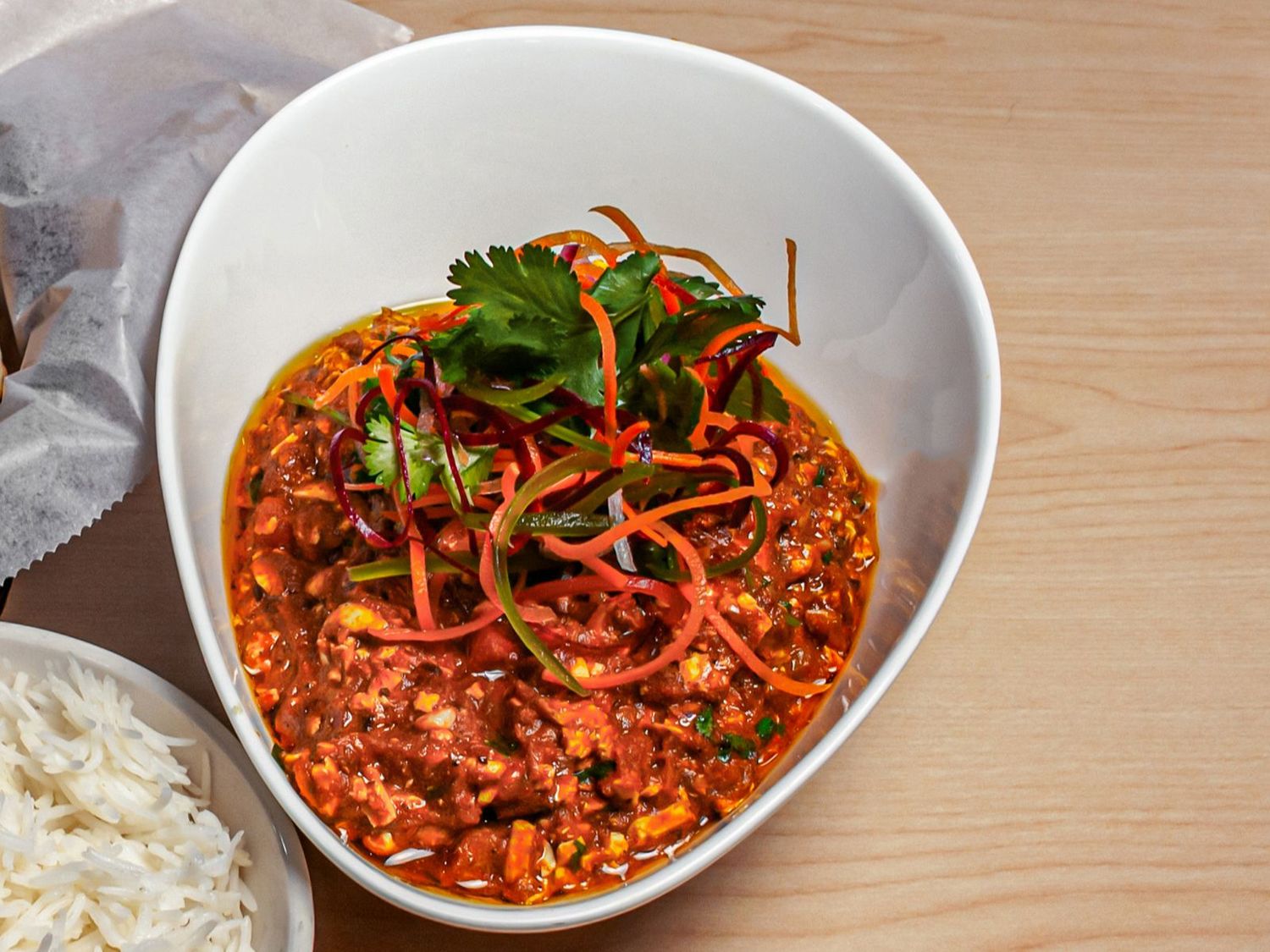A bowl of paneer burji masala under slivered vegetables and coriander, with basmati rice alongside