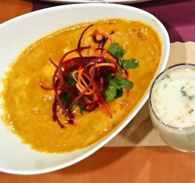 Saffron curry topped with beet and carrot ribbons and cilantro, a lassi alongside