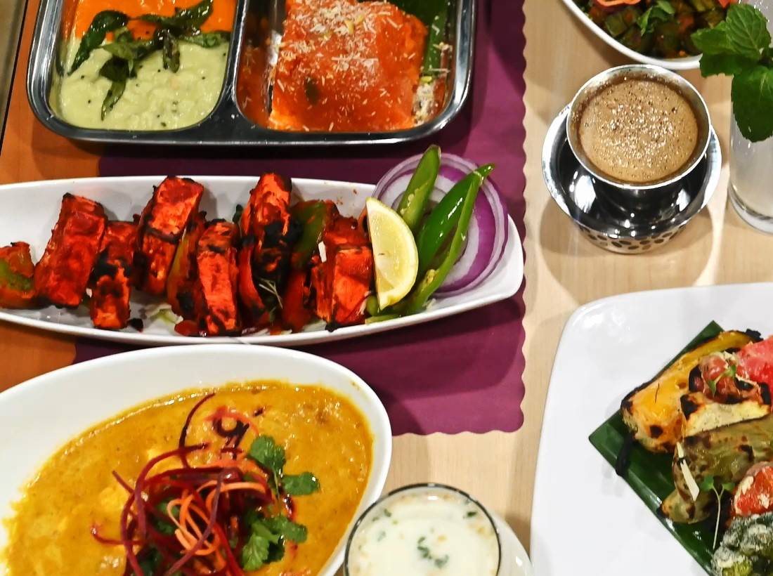 Tandoori paneer tikka skewers with lemon and chillies beside a tray of chutneys
